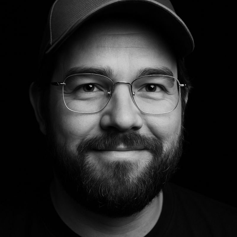 Black-and-white portrait of Olivier Buffon smiling, wearing a cap and glasses